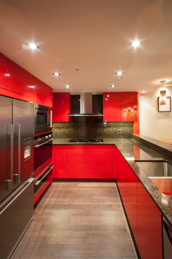 This is an example of a mid-sized eclectic l-shaped eat-in kitchen in Vancouver with a double-bowl sink, flat-panel cabinets, red cabinets, quartz benchtops, black splashback, stainless steel appliances, dark hardwood floors and a peninsula.