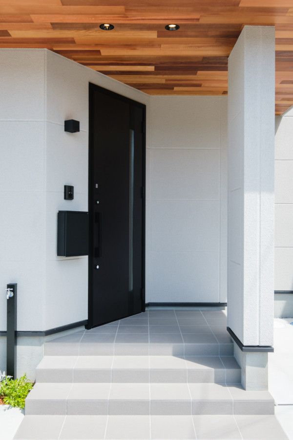 Cette image montre une porte d'entrée avec un mur blanc, une porte simple, une porte noire et un plafond en bois.