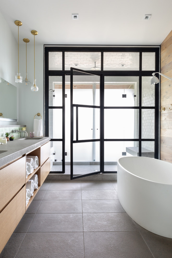 This is an example of a beach style master bathroom in Milwaukee with flat-panel cabinets, light wood cabinets, a freestanding tub, an alcove shower, white tile, subway tile, white walls, grey floor, a hinged shower door and grey benchtops.