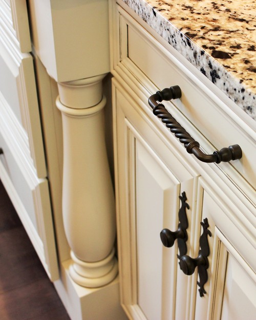 Close-up of a cream raised-panel kitchen cabinet with an oil-rubbed bronze twisted bar pull and decorative latch beneath a speckled granite countertop