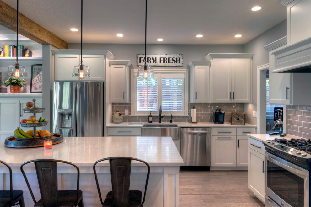 This is an example of a large country l-shaped open plan kitchen in Portland with a farmhouse sink, white cabinets, grey splashback, subway tile splashback, stainless steel appliances, with island and brown floor.
