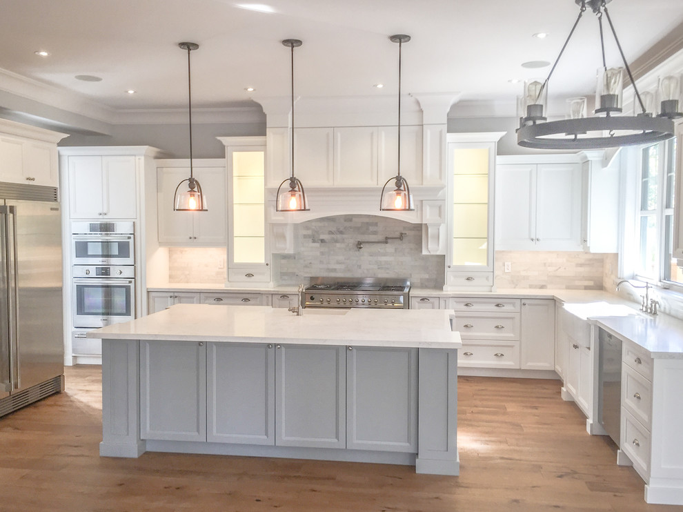 Inspiration for a large country u-shaped eat-in kitchen in Toronto with a farmhouse sink, recessed-panel cabinets, white cabinets, marble benchtops, grey splashback, marble splashback, stainless steel appliances, medium hardwood floors, with island, brown floor and white benchtop.