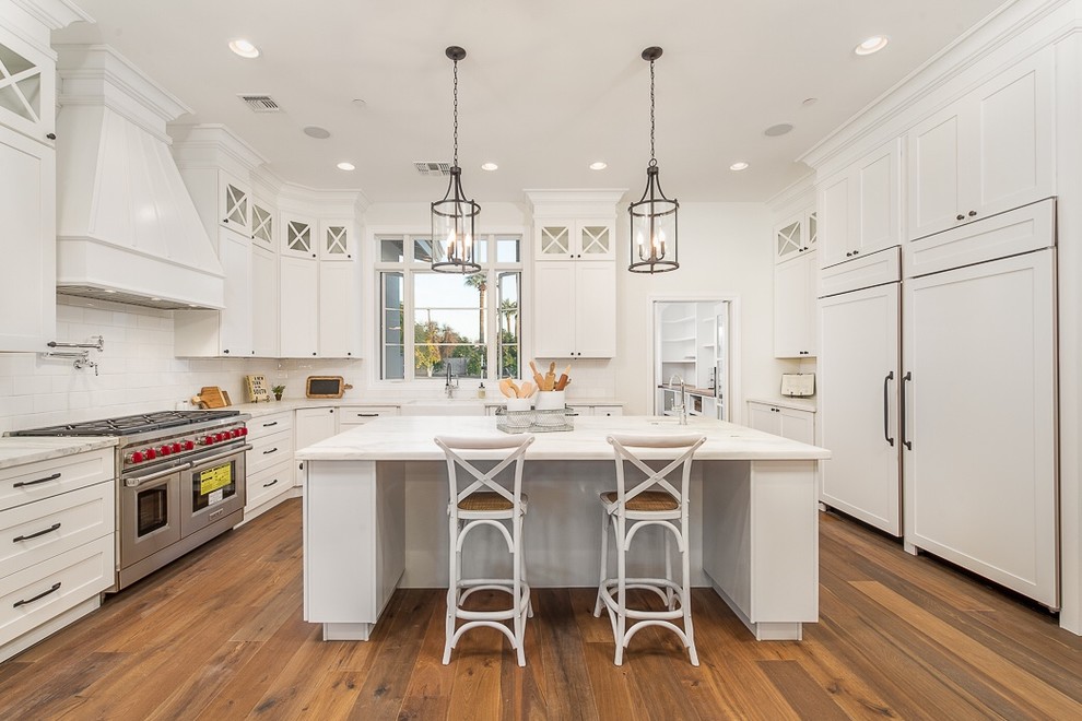Design ideas for an expansive traditional u-shaped kitchen in Phoenix with a farmhouse sink, shaker cabinets, white cabinets, white splashback, subway tile splashback, panelled appliances, medium hardwood floors and with island.