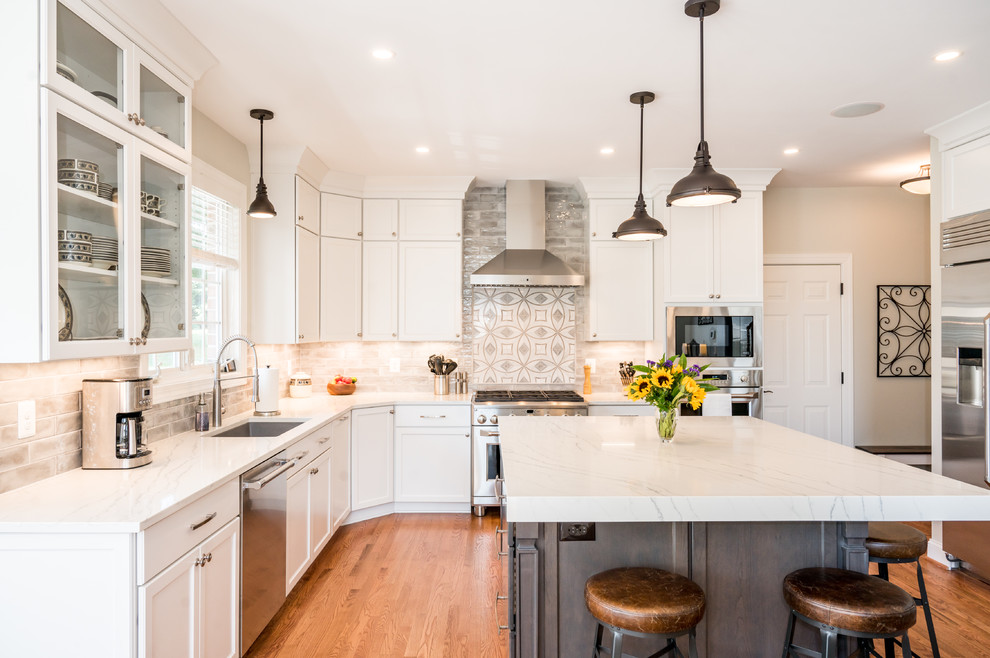 Inspiration for a large transitional u-shaped light wood floor open concept kitchen remodel in Baltimore with an undermount sink, shaker cabinets, white cabinets, quartz countertops, gray backsplash, ceramic backsplash, stainless steel appliances, an island and white countertops