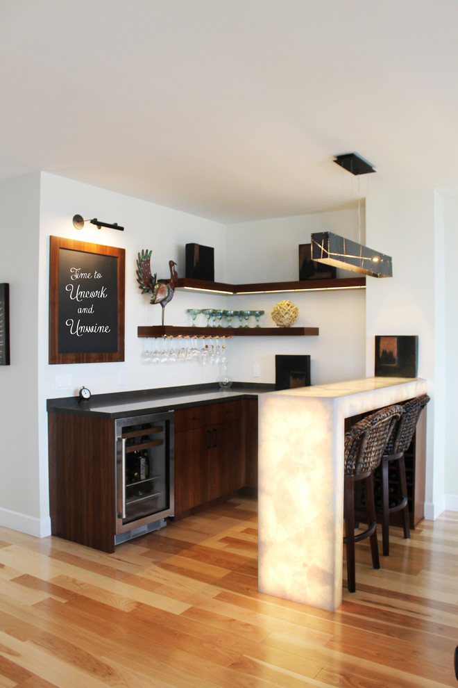 This is an example of a mid-sized contemporary u-shaped seated home bar in Los Angeles with dark wood cabinets, light hardwood floors and flat-panel cabinets.