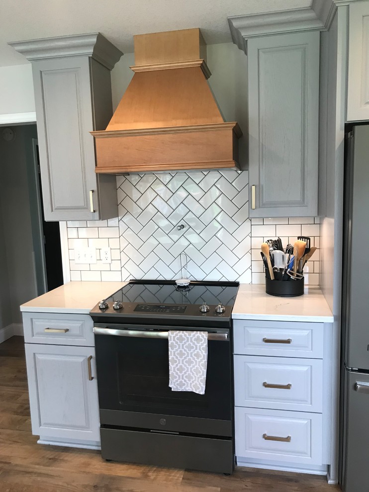 Example of a mid-sized transitional u-shaped vinyl floor and brown floor enclosed kitchen design with an undermount sink, raised-panel cabinets, gray cabinets, quartz countertops, white backsplash, ceramic backsplash, a peninsula and white countertops