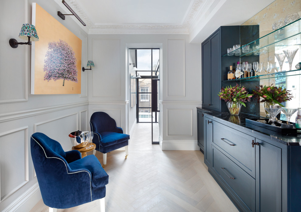 Classic single-wall dry bar in London with shaker cabinets, blue cabinets, mirror splashback and light hardwood flooring.