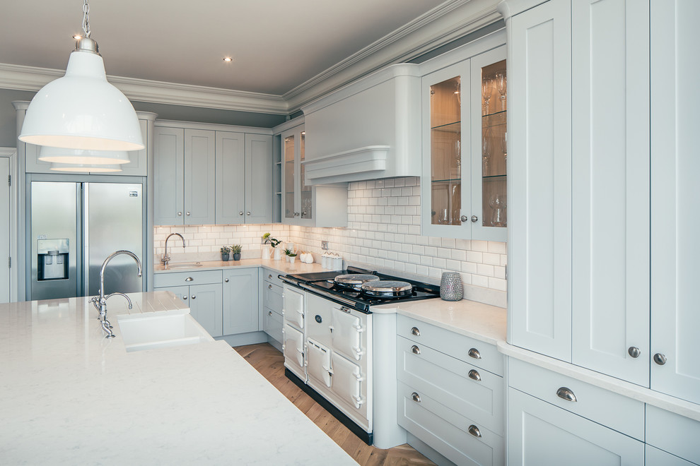 Design ideas for a large transitional l-shaped open plan kitchen in Hertfordshire with a drop-in sink, shaker cabinets, blue cabinets, granite benchtops, white splashback, ceramic splashback, stainless steel appliances, light hardwood floors, with island and beige floor.
