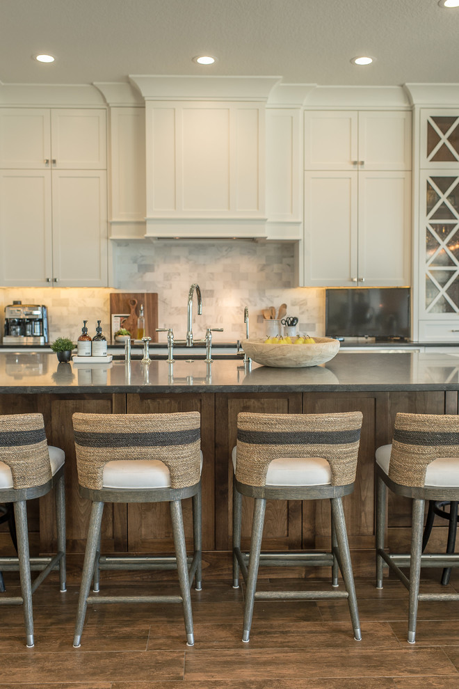 Large beach style l-shaped open plan kitchen in Orlando with an undermount sink, shaker cabinets, white cabinets, granite benchtops, white splashback, subway tile splashback, stainless steel appliances, medium hardwood floors, with island, brown floor and black benchtop.