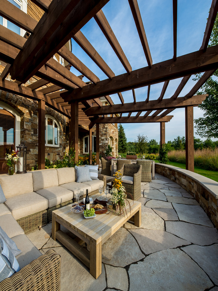 Inspiration for a large country backyard patio in Minneapolis with natural stone pavers and a pergola.