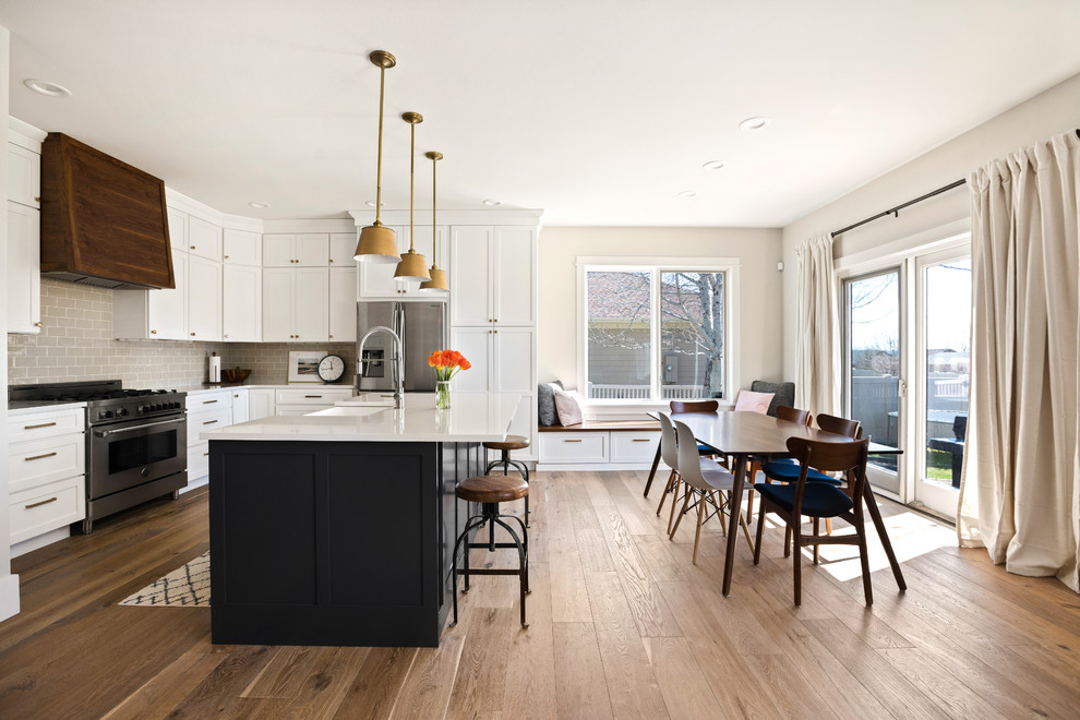 Inspiration for a transitional l-shaped light wood floor and brown floor kitchen remodel with a farmhouse sink, shaker cabinets, white cabinets, quartz countertops, white backsplash, subway tile backsplash, stainless steel appliances, an island and white countertops