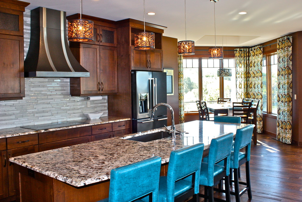 Open concept kitchen - large transitional l-shaped medium tone wood floor and brown floor open concept kitchen idea with an undermount sink, recessed-panel cabinets, medium tone wood cabinets, granite countertops, white backsplash, glass tile backsplash, stainless steel appliances and an island