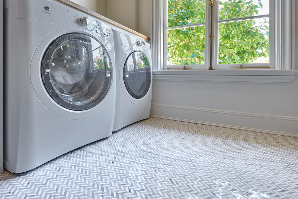 Inspiration for a transitional laundry room in New York with glass benchtops and marble floors.