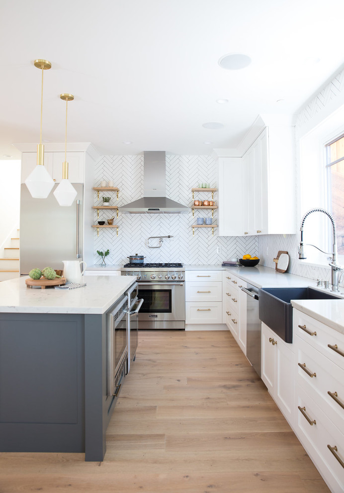 Photo of a transitional l-shaped kitchen in San Francisco with a farmhouse sink, shaker cabinets, white cabinets, quartz benchtops, white splashback, stainless steel appliances, light hardwood floors, with island, beige floor and white benchtop.