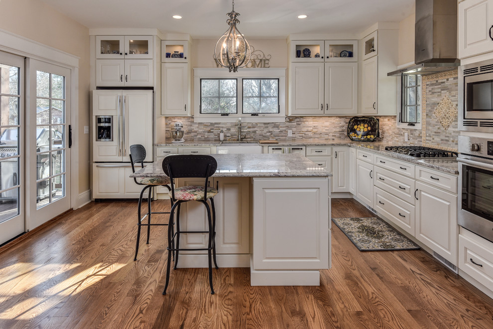 Inspiration for a large transitional l-shaped medium tone wood floor kitchen remodel with a farmhouse sink, raised-panel cabinets, white cabinets, granite countertops, multicolored backsplash, matchstick tile backsplash, stainless steel appliances and an island