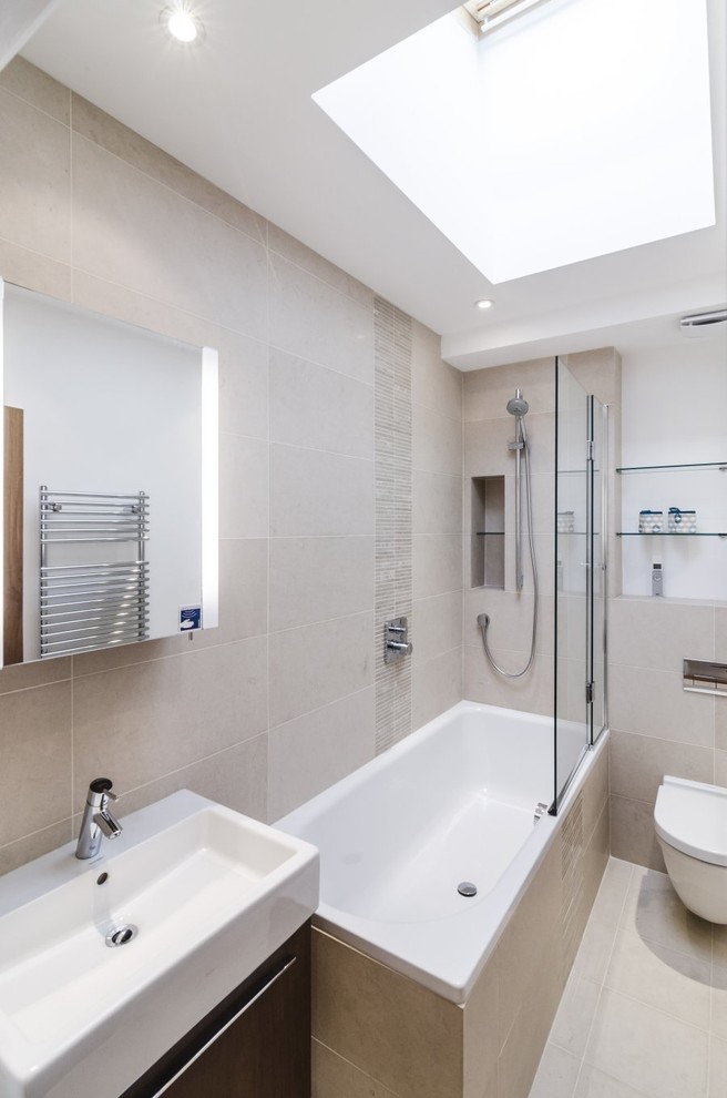 This is an example of a mid-sized modern master bathroom in London with a wall-mount sink, flat-panel cabinets, dark wood cabinets, a drop-in tub, a shower/bathtub combo, a wall-mount toilet, beige tile, porcelain tile, beige walls and porcelain floors.