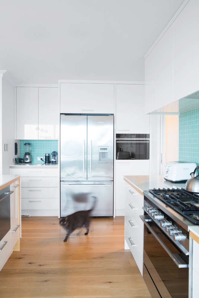 Inspiration for a mid-sized scandinavian u-shaped eat-in kitchen in Auckland with a double-bowl sink, flat-panel cabinets, white cabinets, blue splashback, mosaic tile splashback, stainless steel appliances, light hardwood floors and with island.