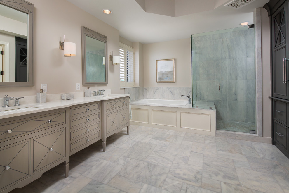Photo of a large beach style master bathroom in Miami with furniture-like cabinets, grey cabinets, a drop-in tub, gray tile, stone tile, beige walls, marble floors, an undermount sink and engineered quartz benchtops.