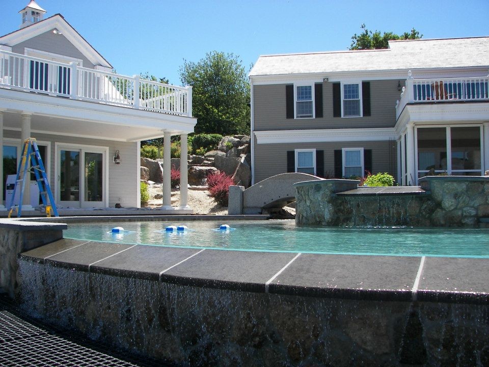 Hot tub - large rustic backyard stone and custom-shaped infinity hot tub idea in Boston