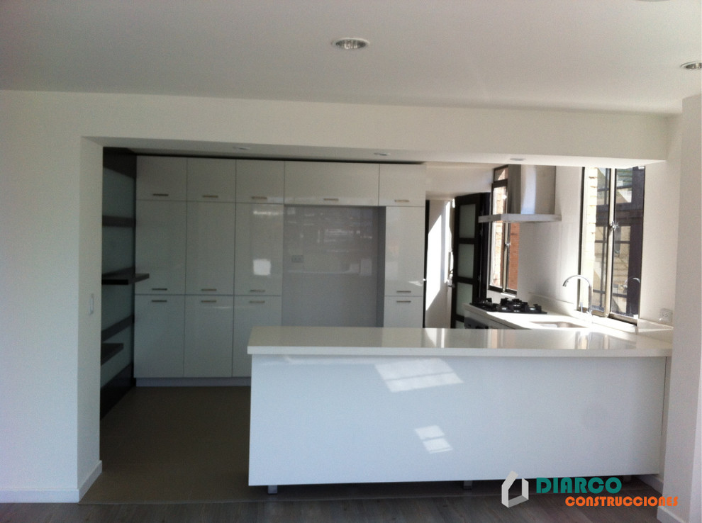 This is an example of a mid-sized modern l-shaped open plan kitchen in Other with a single-bowl sink, flat-panel cabinets, white cabinets, tile benchtops, white appliances, ceramic floors and a peninsula.