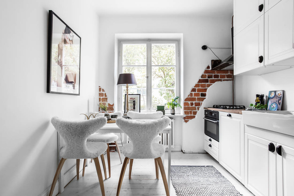 Mid-sized scandinavian single-wall eat-in kitchen in Stockholm with white floor, a farmhouse sink, raised-panel cabinets, white cabinets, black appliances, painted wood floors and no island.