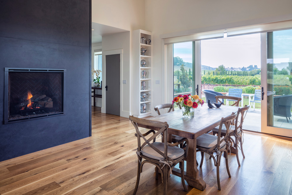 Photo of a transitional dining room in San Francisco with white walls, medium hardwood floors and a metal fireplace surround.