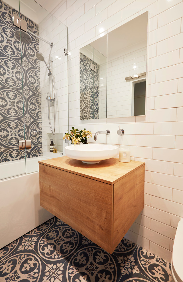 Inspiration for a small contemporary master bathroom in Sydney with medium wood cabinets, a freestanding tub, a shower/bathtub combo, a wall-mount toilet, blue tile, ceramic tile, white walls, ceramic floors, a vessel sink, wood benchtops and brown benchtops.