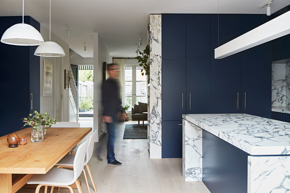This is an example of a mid-sized modern l-shaped eat-in kitchen in Melbourne with an undermount sink, flat-panel cabinets, blue cabinets, marble benchtops, white splashback, marble splashback, stainless steel appliances, light hardwood floors, with island and white benchtop.