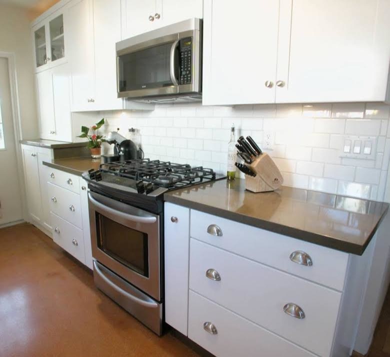 Photo of a mid-sized traditional l-shaped kitchen in San Diego with shaker cabinets, white cabinets, solid surface benchtops, white splashback, subway tile splashback, stainless steel appliances, concrete floors and orange floor.