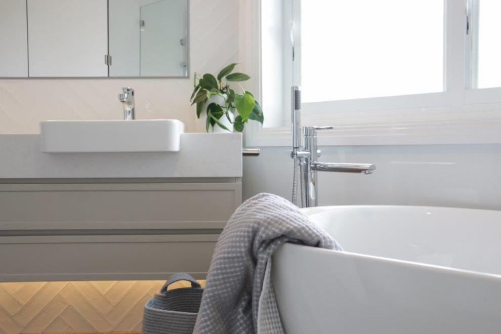 Источник вдохновения для домашнего уюта: главная ванная комната среднего размера в современном стиле с фасадами в стиле шейкер, серыми фасадами, отдельно стоящей ванной, открытым душем, унитазом-моноблоком, белой плиткой, керамогранитной плиткой, белыми стенами, полом из цементной плитки, столешницей из искусственного кварца, серым полом, открытым душем, белой столешницей, тумбой под две раковины и подвесной тумбой
