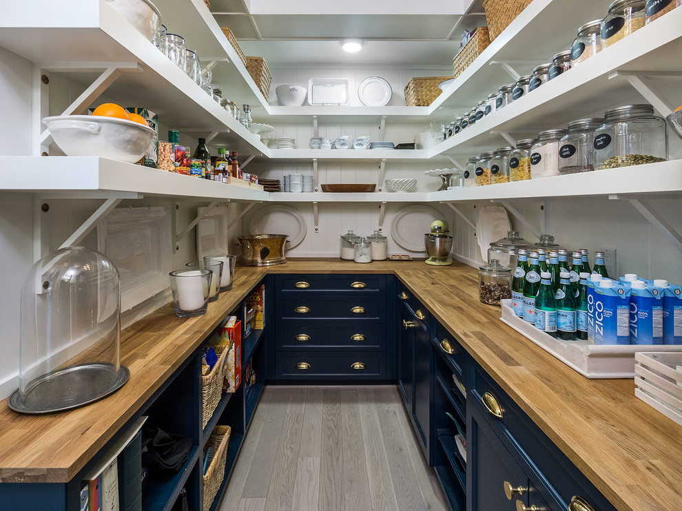 This is an example of a country u-shaped kitchen pantry in Portland with recessed-panel cabinets, blue cabinets, wood benchtops, light hardwood floors, grey floor and brown benchtop.