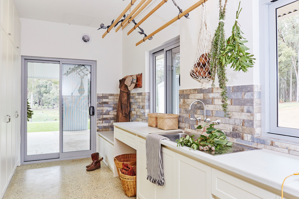 This is an example of a large transitional galley dedicated laundry room in Other with a single-bowl sink, shaker cabinets, white cabinets, laminate benchtops, white walls, concrete floors, grey floor and grey benchtop.