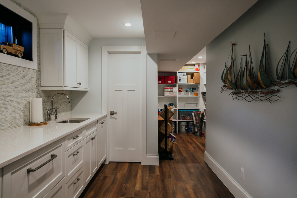 Expansive transitional single-wall dedicated laundry room in Denver with an undermount sink, shaker cabinets, white cabinets, quartz benchtops, grey walls, vinyl floors, a stacked washer and dryer, brown floor and white benchtop.