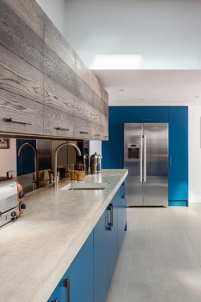 Photo of a large industrial u-shaped eat-in kitchen in Other with a double-bowl sink, flat-panel cabinets, blue cabinets, concrete benchtops, metallic splashback, glass sheet splashback, stainless steel appliances and porcelain floors.