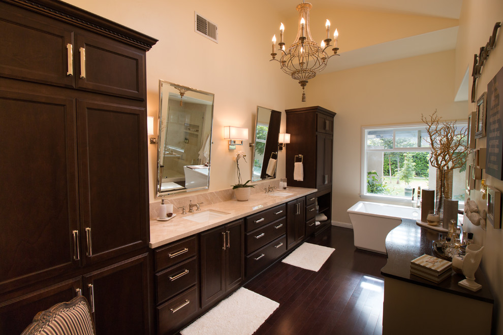Photo of an expansive transitional master bathroom in Other with recessed-panel cabinets, dark wood cabinets, a freestanding tub, a two-piece toilet, yellow tile, porcelain tile, yellow walls, dark hardwood floors, an undermount sink, marble benchtops, brown floor and a hinged shower door.