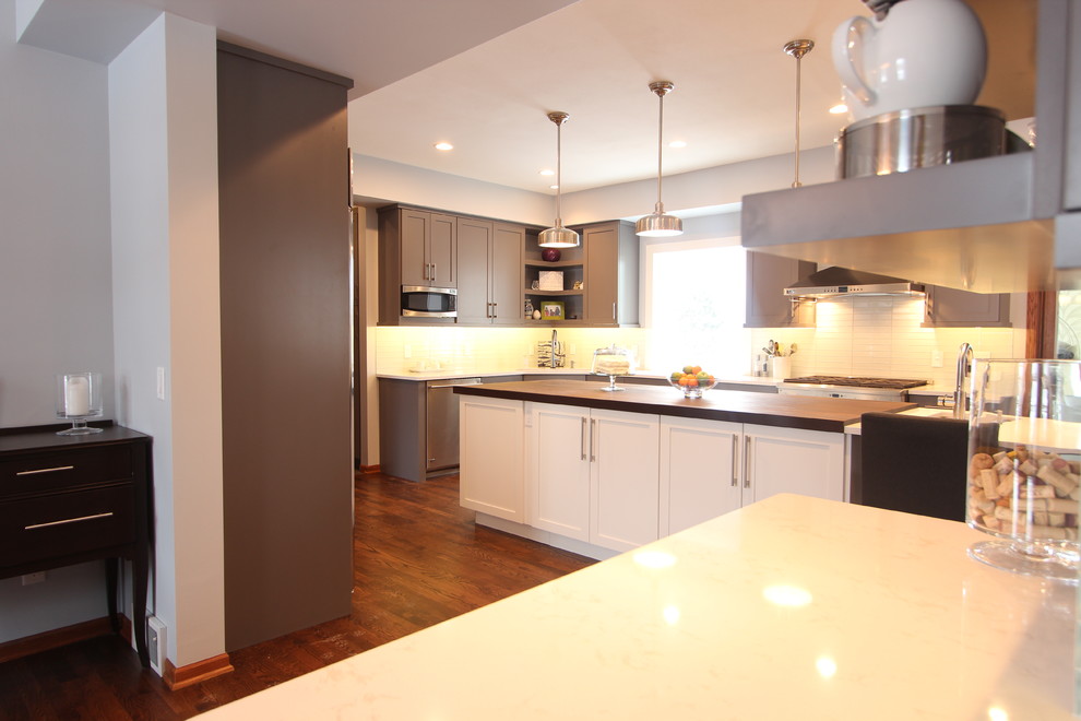 Large transitional u-shaped medium tone wood floor open concept kitchen photo with an undermount sink, shaker cabinets, gray cabinets, quartz countertops, white backsplash, glass tile backsplash, stainless steel appliances and an island