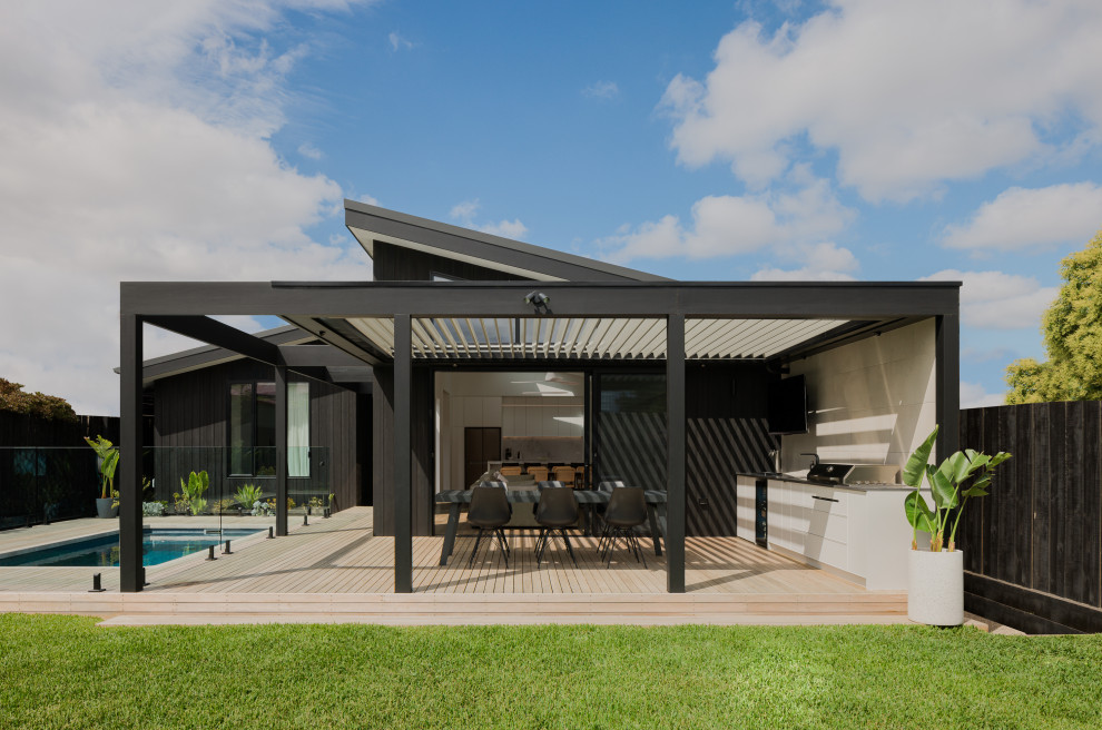 Idée de décoration pour une grande terrasse arrière et au rez-de-chaussée minimaliste avec une cuisine d'été, une pergola et un garde-corps en verre.