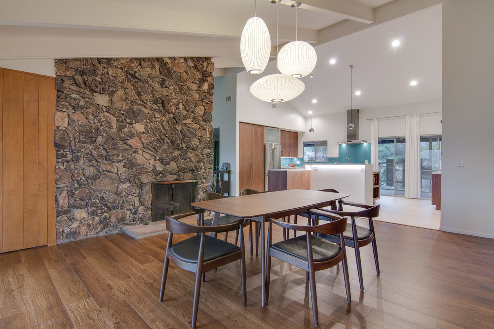 Photo of a midcentury open plan dining in Tampa with white walls, dark hardwood floors, a standard fireplace and a stone fireplace surround.