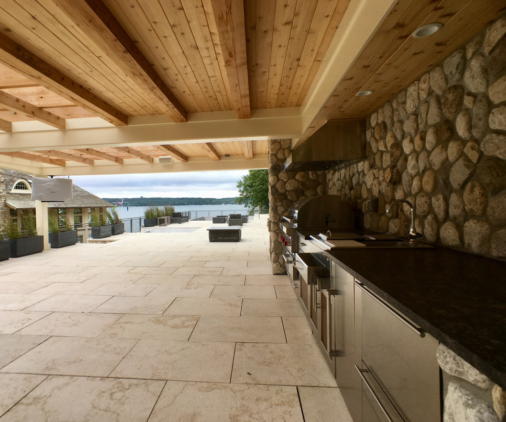 This is an example of an expansive traditional side yard patio in Milwaukee with an outdoor kitchen and a roof extension.