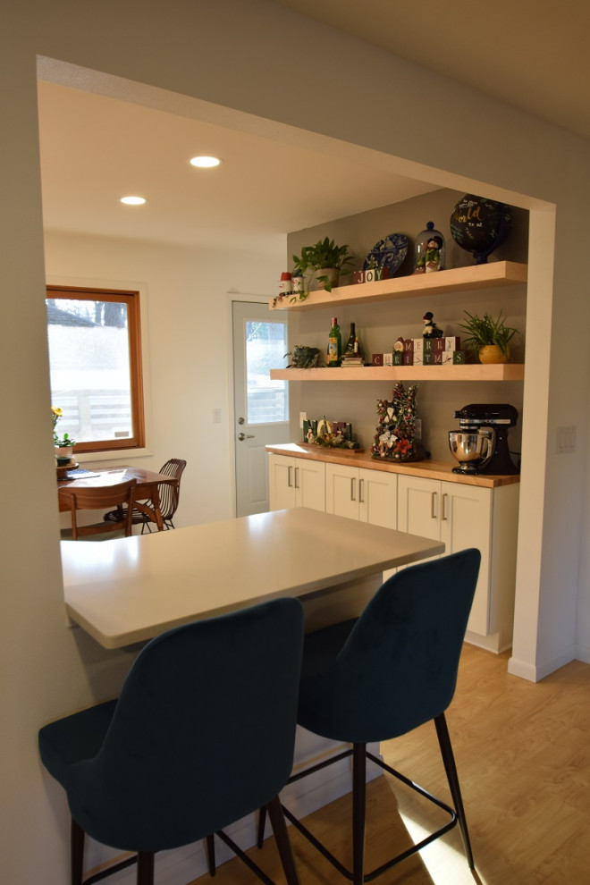 Example of a galley vinyl floor kitchen design with an undermount sink, shaker cabinets, light wood cabinets, quartz countertops, stainless steel appliances and white countertops