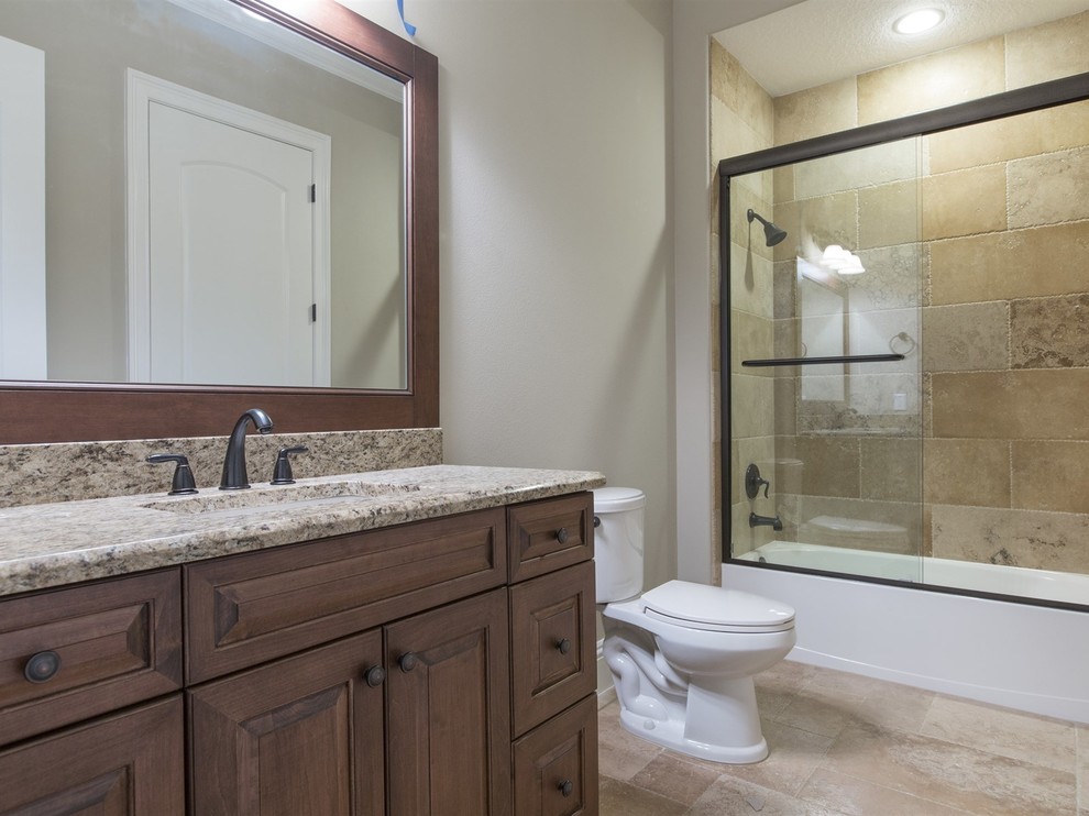 Mid-sized mediterranean bathroom in Orlando with raised-panel cabinets, dark wood cabinets, an alcove tub, a shower/bathtub combo, a two-piece toilet, beige tile, brown tile, stone tile, white walls, porcelain floors, an undermount sink and granite benchtops.
