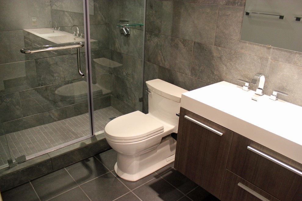 This is an example of a small modern bathroom in Other with a wall-mount sink, flat-panel cabinets, medium wood cabinets, solid surface benchtops, an alcove shower, a one-piece toilet, gray tile, porcelain tile, grey walls and porcelain floors.