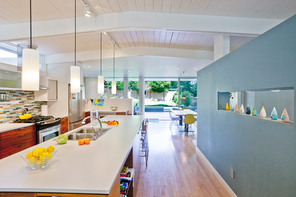 Photo of a modern galley eat-in kitchen in Seattle with a drop-in sink, flat-panel cabinets, dark wood cabinets, laminate benchtops, multi-coloured splashback, glass tile splashback and stainless steel appliances.