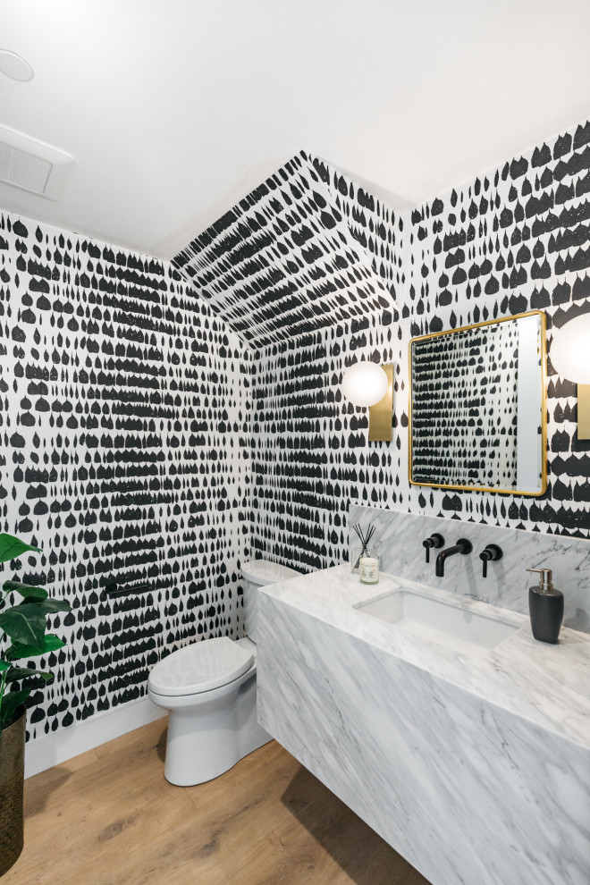 This is an example of a small country powder room in Los Angeles with black and white tile, an undermount sink, marble benchtops, multi-coloured walls, medium hardwood floors, brown floor, grey benchtops and wallpaper.
