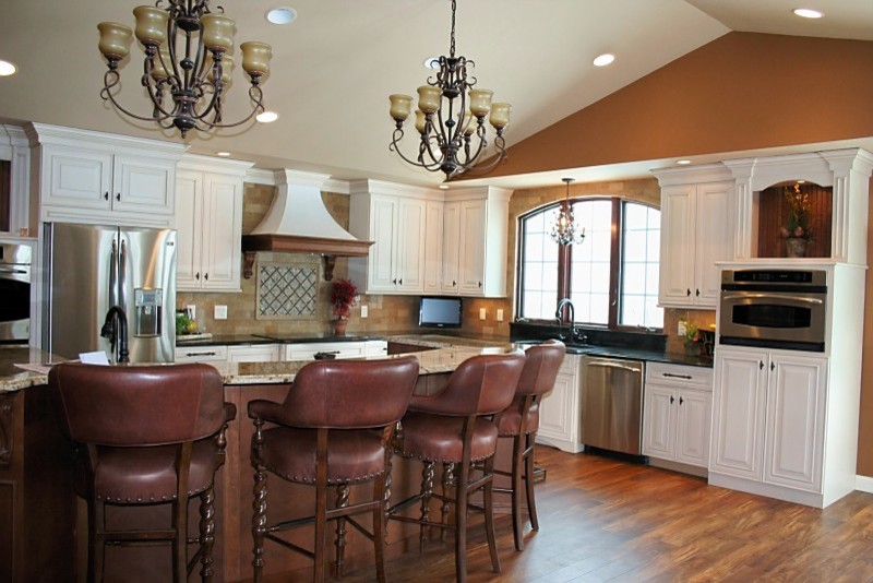 Design ideas for a mid-sized traditional l-shaped eat-in kitchen in Cedar Rapids with an undermount sink, raised-panel cabinets, white cabinets, granite benchtops, beige splashback, stone tile splashback, stainless steel appliances, medium hardwood floors, with island and brown floor.