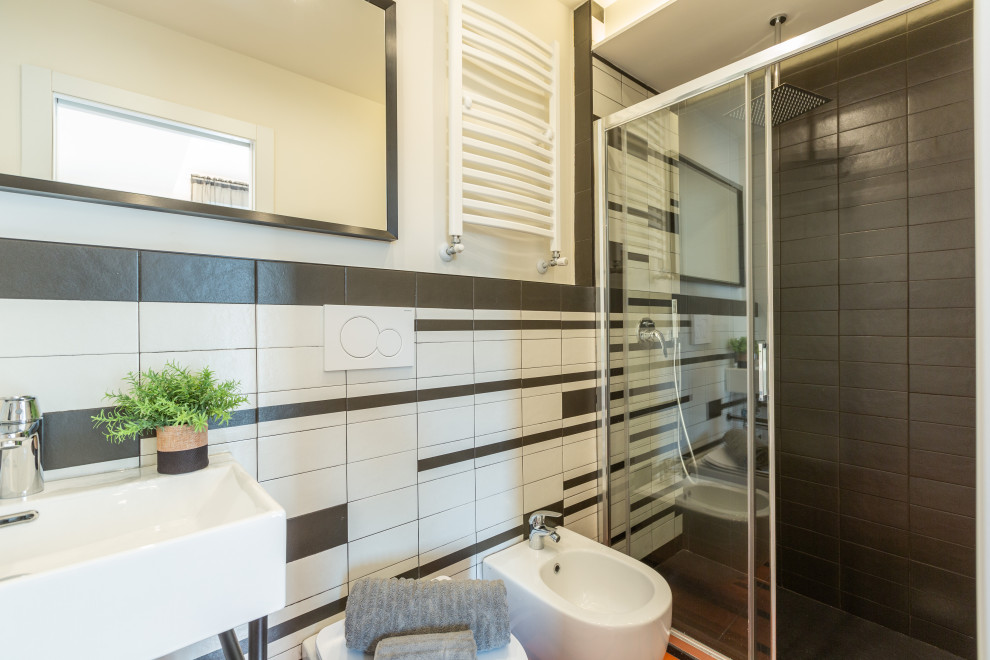 Small midcentury bathroom in Milan with a built-in shower, a wall mounted toilet, black and white tiles, ceramic tiles, beige walls, ceramic flooring, a trough sink, multi-coloured floors, a single sink and a floating vanity unit.