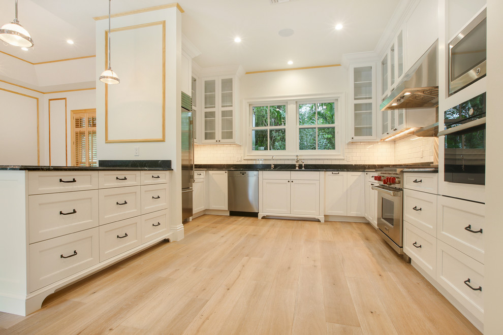 Inspiration for a mid-sized beach style u-shaped eat-in kitchen in Miami with a drop-in sink, white cabinets, quartzite benchtops, white splashback, subway tile splashback, stainless steel appliances, light hardwood floors and with island.