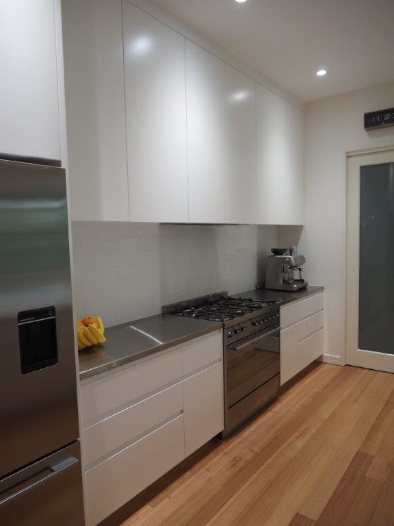 Photo of a large contemporary galley open plan kitchen in Brisbane with a double-bowl sink, flat-panel cabinets, white cabinets, quartz benchtops, white splashback, ceramic splashback, stainless steel appliances, medium hardwood floors, with island and brown floor.
