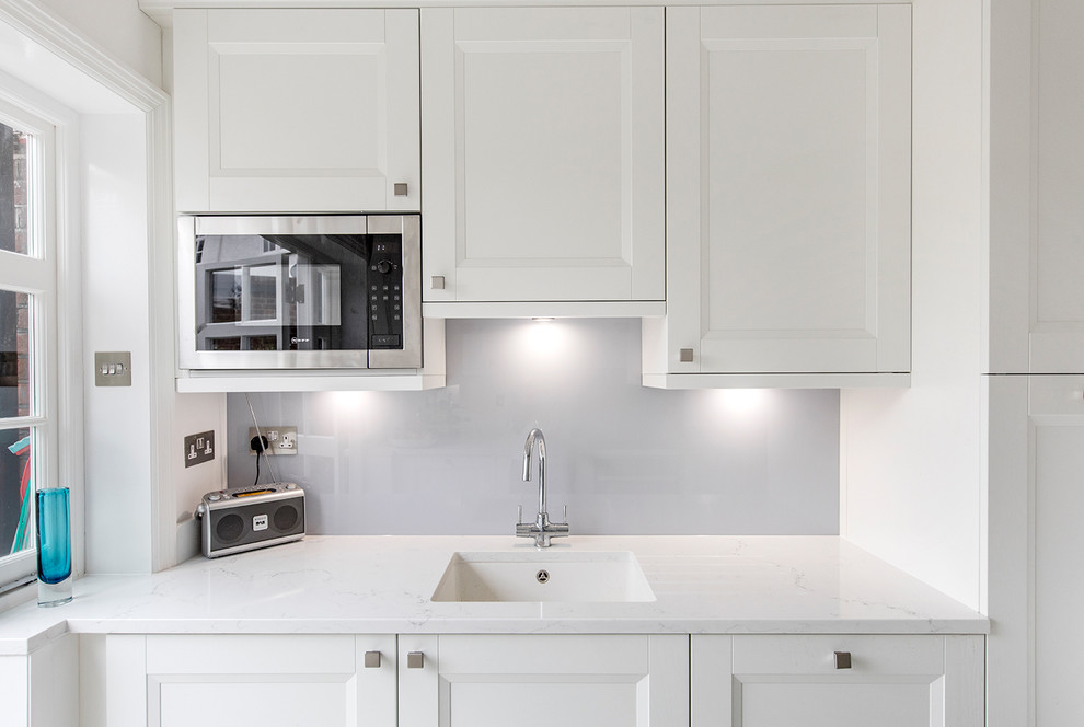 Design ideas for a small transitional galley separate kitchen in London with white cabinets, blue splashback, no island, an undermount sink, shaker cabinets, quartzite benchtops, glass sheet splashback and black appliances.