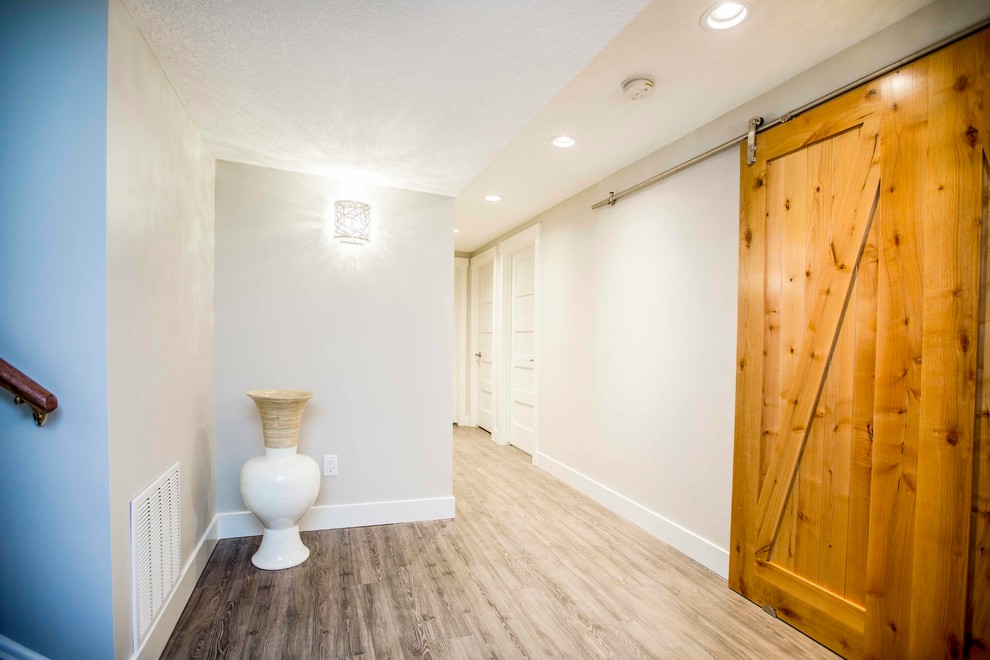 Inspiration for a large rustic look-out light wood floor basement remodel in Calgary with white walls, a standard fireplace and a brick fireplace